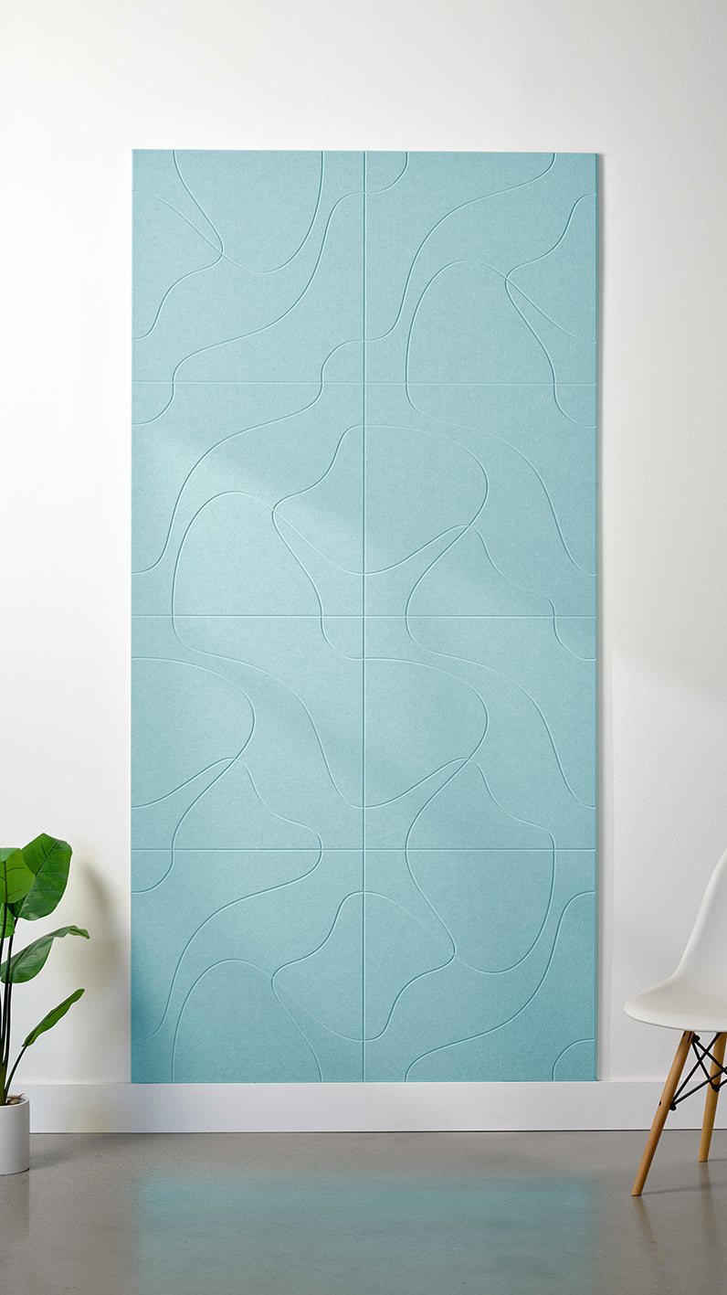 Baby blue Felt Right 4’ x 8’ PET felt panel with flowing lines similar to a topographical map engraved into the material against a white wall. A plant and chair are in the foreground.