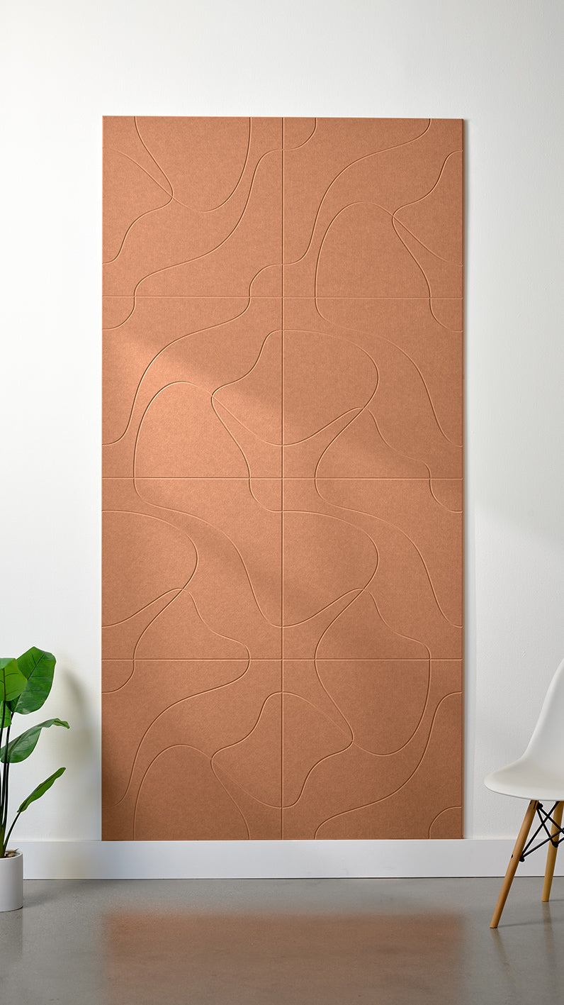 Light orange Felt Right 4’ x 8’ PET felt panel with flowing lines similar to a topographical map engraved into the material against a white wall. A plant and chair are in the foreground.