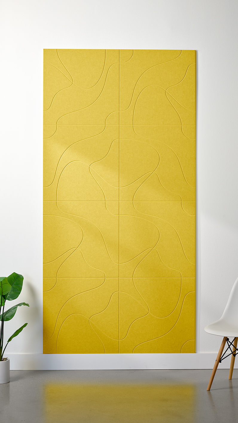 Bright yellow Felt Right 4’ x 8’ PET felt panel with flowing lines similar to a topographical map engraved into the material against a white wall. A plant and chair are in the foreground.