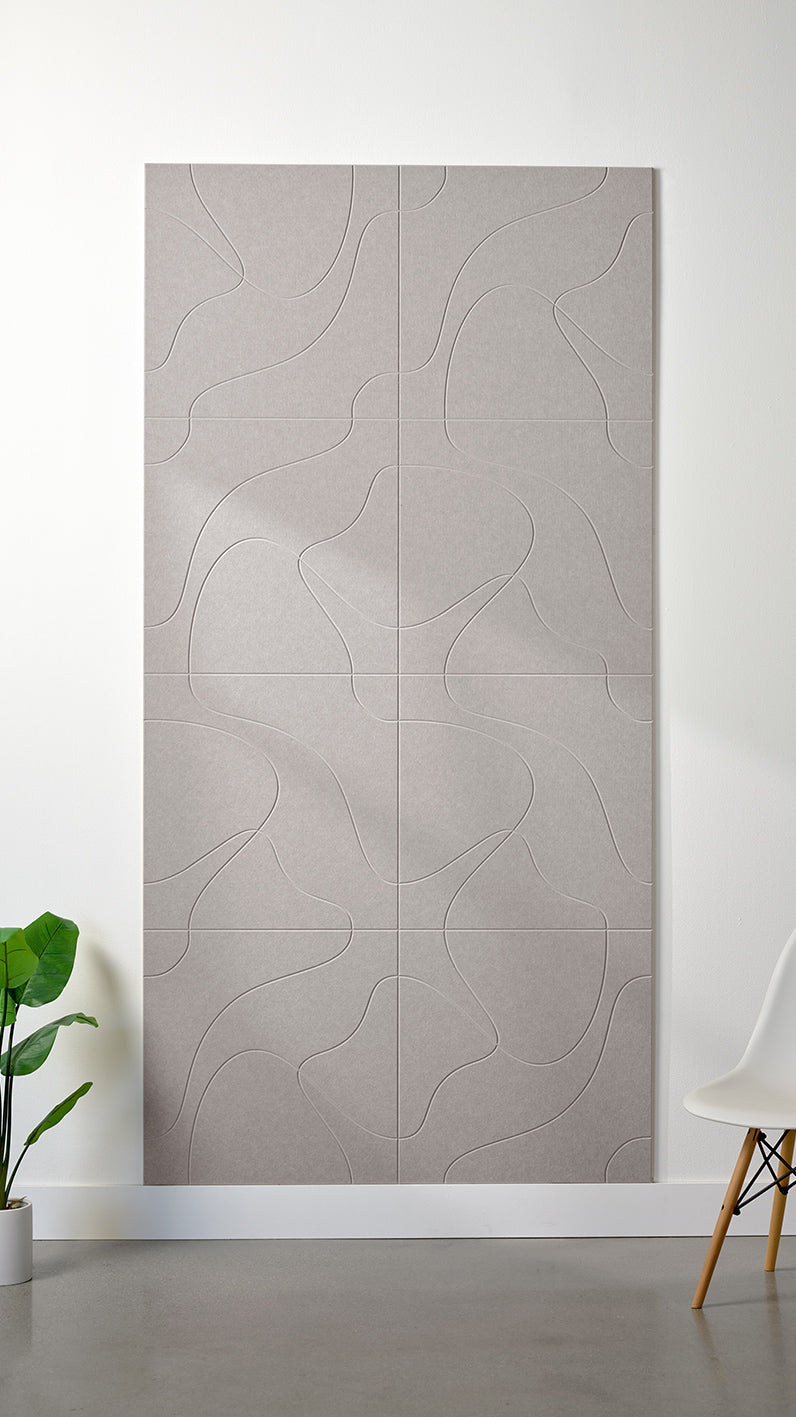 Light grey Felt Right 4’ x 8’ PET felt panel with flowing lines similar to a topographical map engraved into the material against a white wall. A plant and chair are in the foreground.