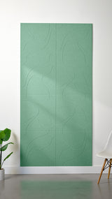 Mint green Felt Right 4’ x 8’ PET felt panel with flowing lines similar to a topographical map engraved into the material against a white wall. A plant and chair are in the foreground.