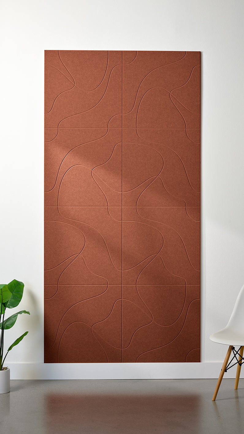 Burnt orange Felt Right 4’ x 8’ PET felt panel with flowing lines similar to a topographical map engraved into the material against a white wall. A plant and chair are in the foreground.