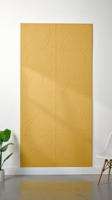 Yellow Felt Right 4’ x 8’ PET felt panel with flowing lines similar to a topographical map engraved into the material against a white wall. A plant and chair are in the foreground.