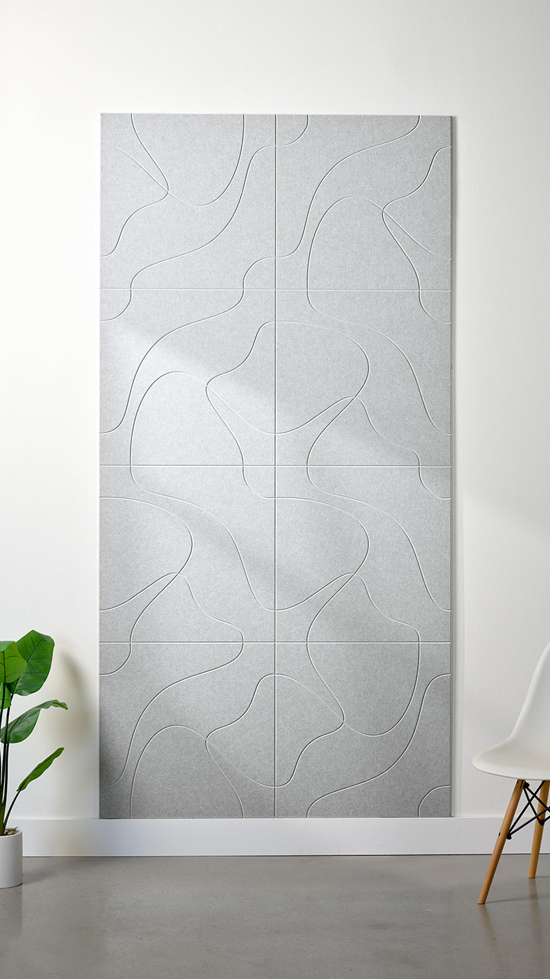 Heathered grey Felt Right 4’ x 8’ PET felt panel with flowing lines similar to a topographical map engraved into the material against a white wall. A plant and chair are in the foreground.