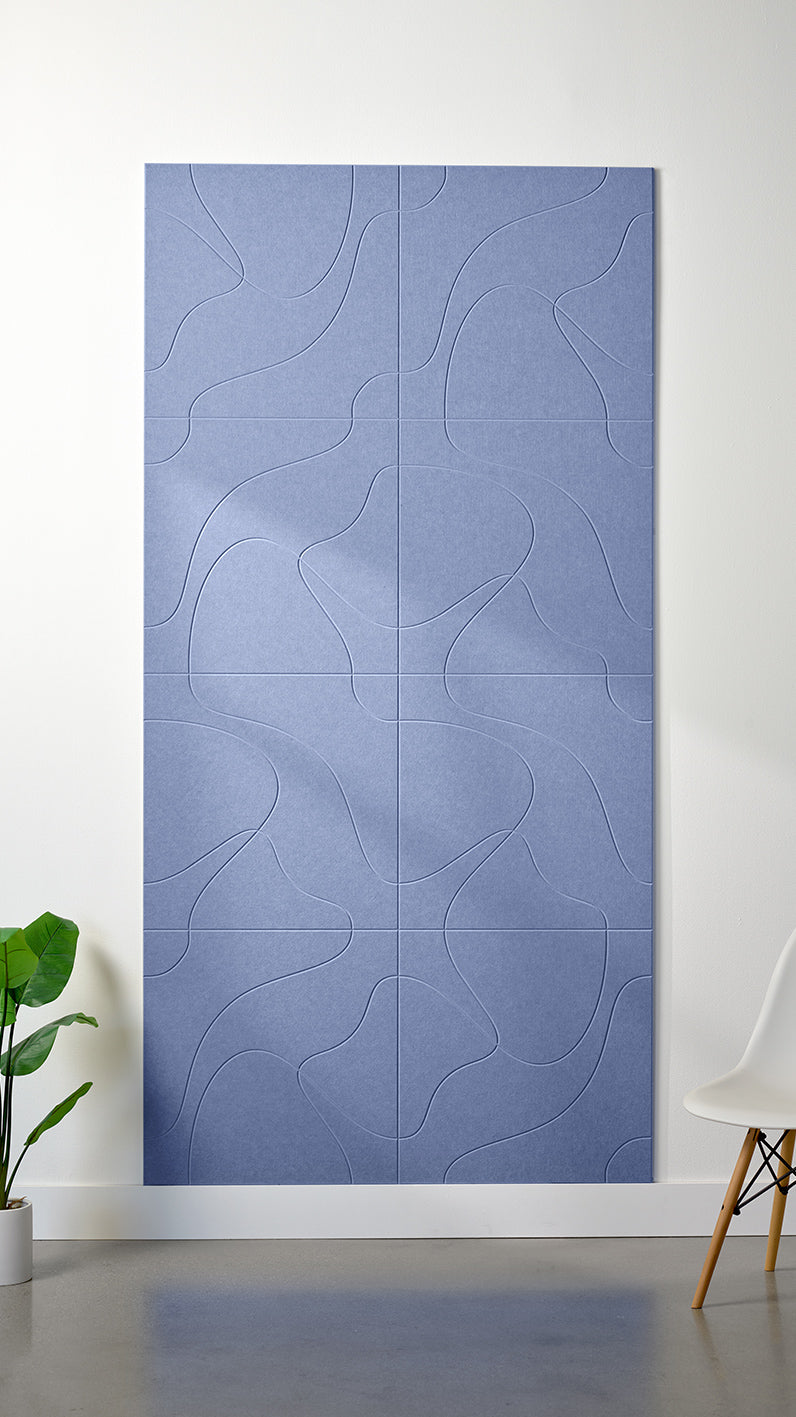 Periwinkle Felt Right 4’ x 8’ PET felt panel with flowing lines similar to a topographical map engraved into the material against a white wall. A plant and chair are in the foreground.