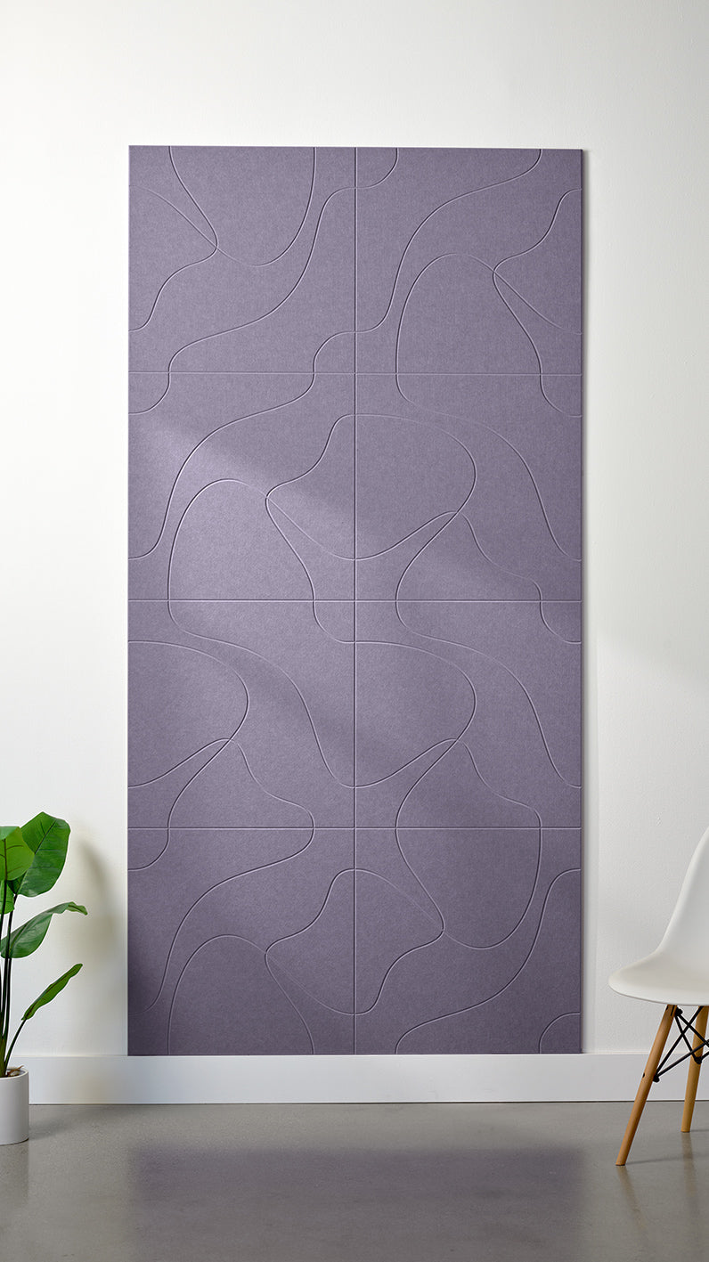 Light purple Felt Right 4’ x 8’ PET felt panel with flowing lines similar to a topographical map engraved into the material against a white wall. A plant and chair are in the foreground.