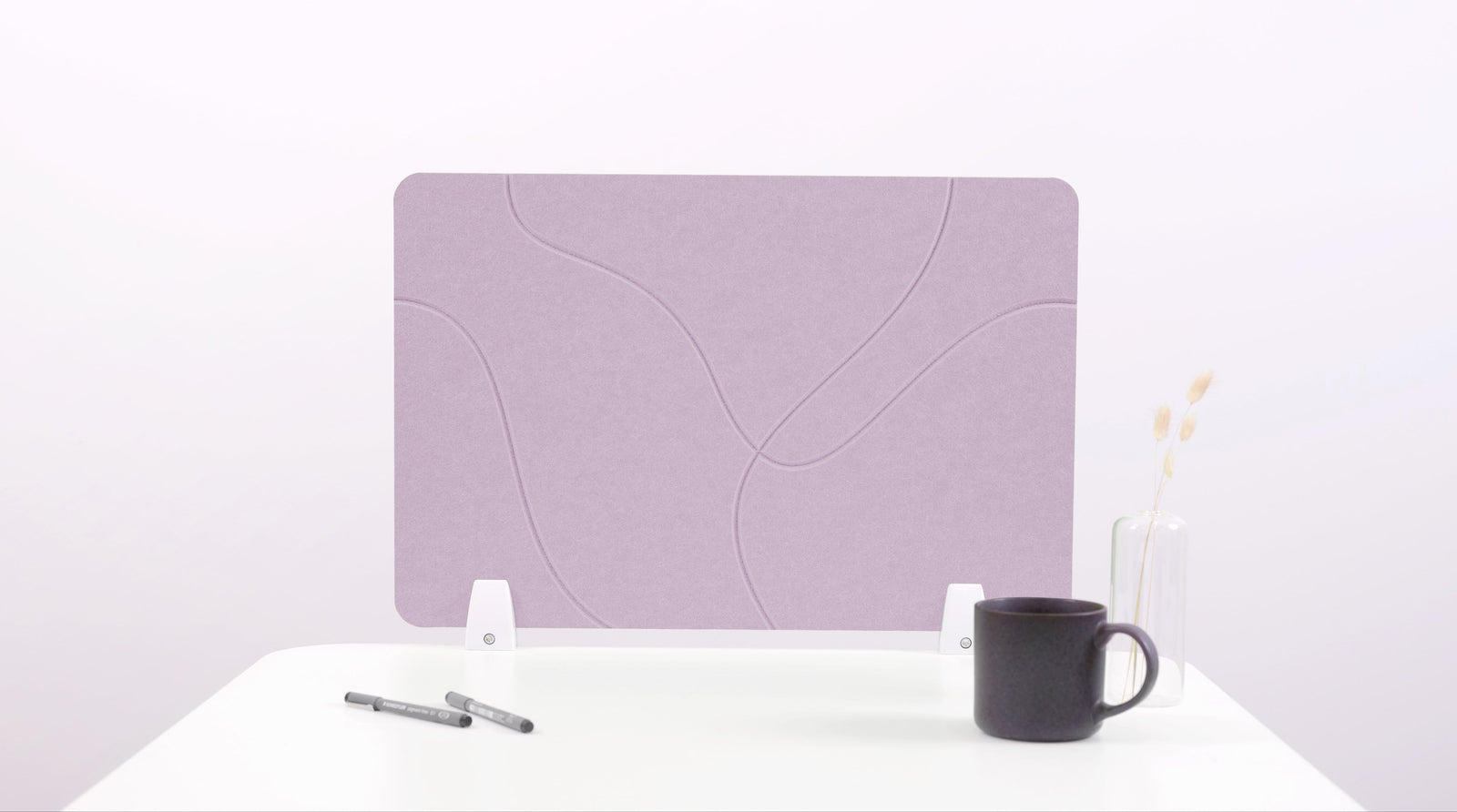 A lilac-colored felt desk divider placed on a desk with a pen and a mug on its surface.
