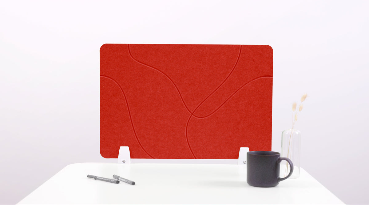 A red felt desk divider with lines placed on a white desk, with a black pen and a cup on its surface.