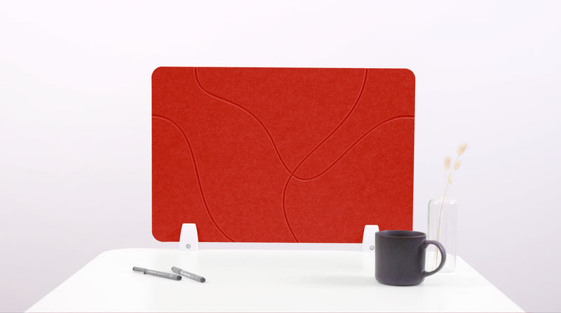 A red felt desk divider with lines placed on a white desk, with a black pen and a cup on its surface.