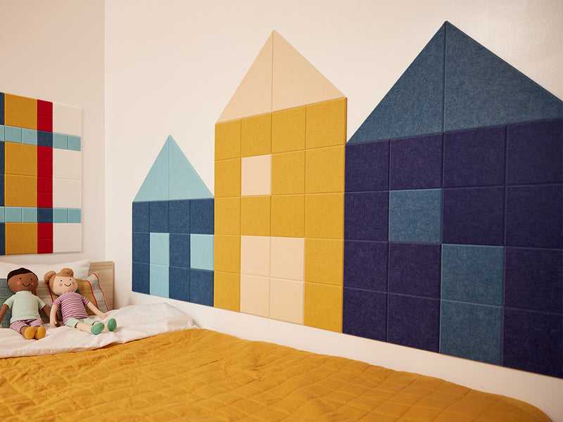 Felt Right wall art design to look like three houses in a row in shades of blue, yellow, and purple felt tiles in a kids bedroom along the bedside of the kids bed
