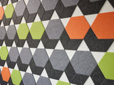 A Felt Right wall art design in shades of grey, orange, and green in a hexagon shapes on a white wall