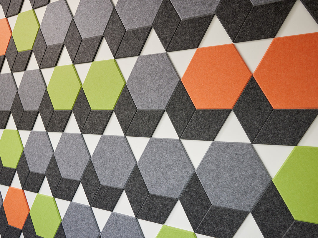 A Felt Right wall art design in shades of grey, orange, and green in a hexagon shapes on a white wall
