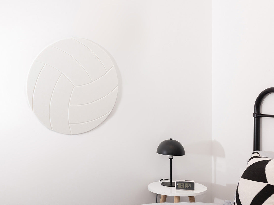 Modern interior with a round white volleyball pinboard, black table lamp, and decorative pillow on a bed.