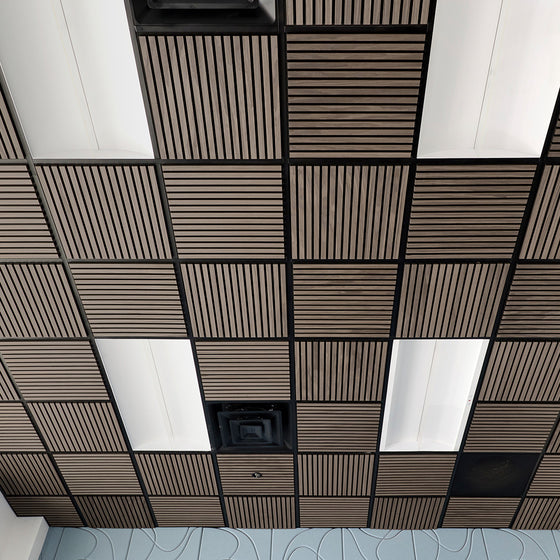 A ceiling grid of square acoustic tiles, featuring alternating dark brown wood-grain slatted panels and white rectangular panels, with black metal grout lines.