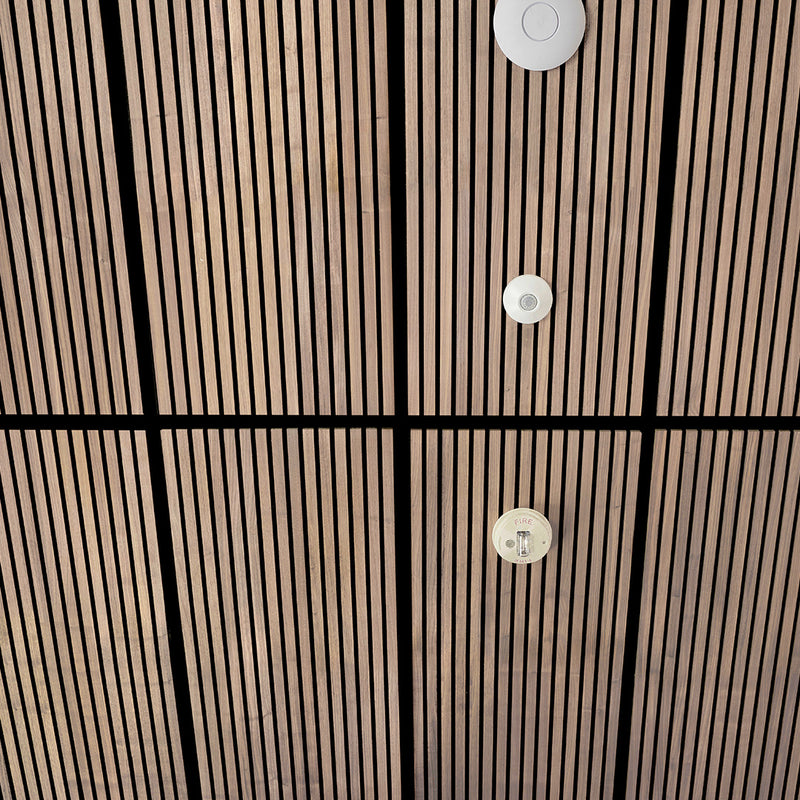 A close-up view of a dark brown slatted ceiling with black grid lines and three white circular smoke detectors mounted vertically.