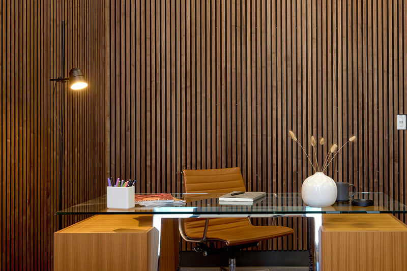 Modern office desk with chair against a wooden paneled wall.