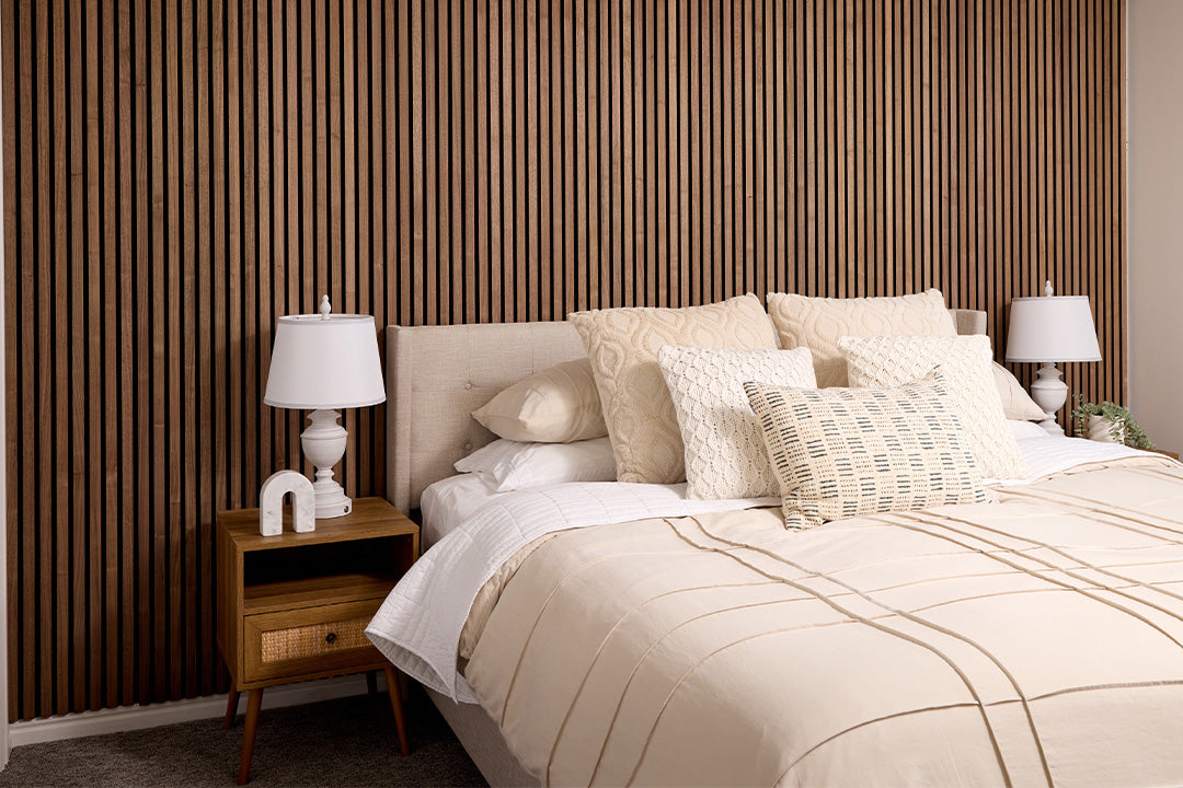 Neatly made bed with decorative pillows in a bedroom setting with a Walnut wood slatted wall