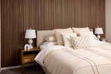 Neatly made bed with decorative pillows in a bedroom setting with a Walnut wood slatted wall