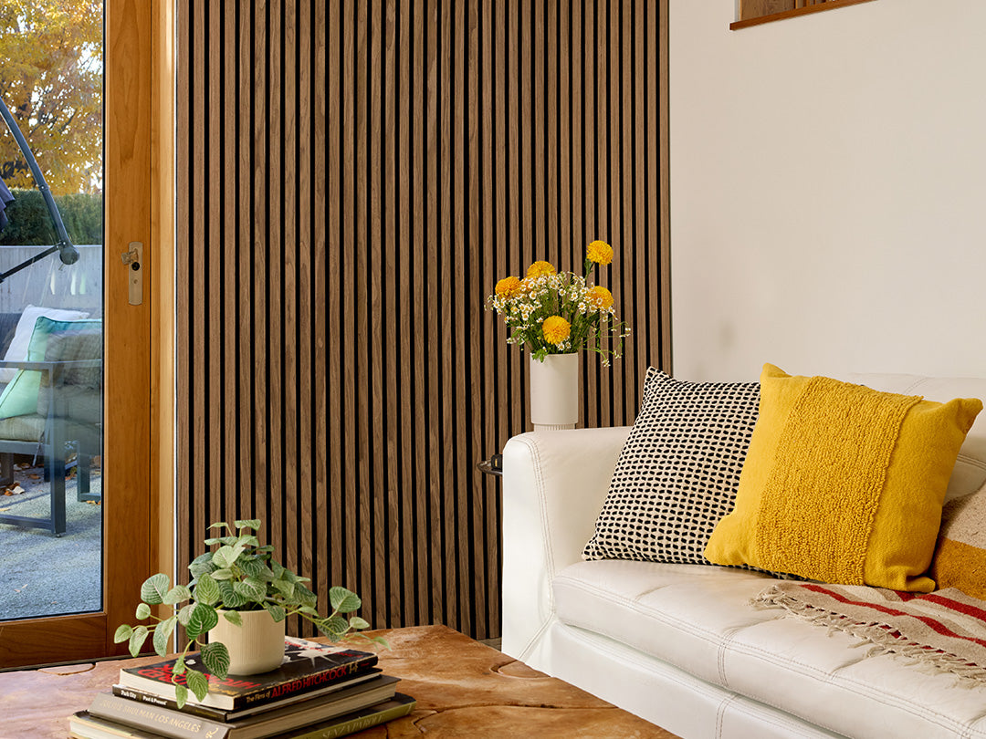 Walnut wood slats behind couch with yellow pillow and plant.