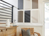 Six fabric sample swatches in neutral tones displayed on white wall above wooden furniture.