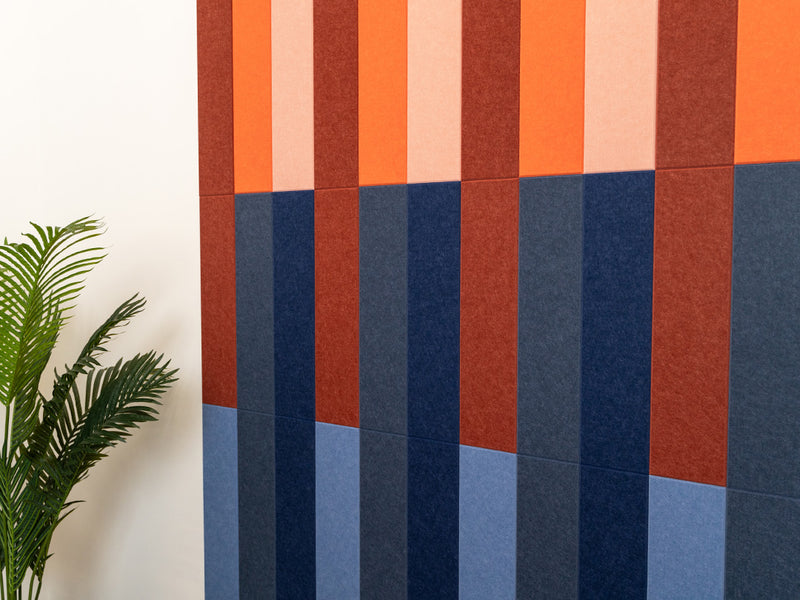 A Felt Right wall art design in shades of blue red and orange on a white wall next to a house plant.