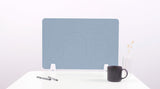 Blue desk divider with wave cutout pattern mounted on white desk with pens and mug.