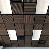 A ceiling grid of square acoustic tiles, featuring alternating dark brown slatted panels and white rectangular panels, with a black metal frame throughout.