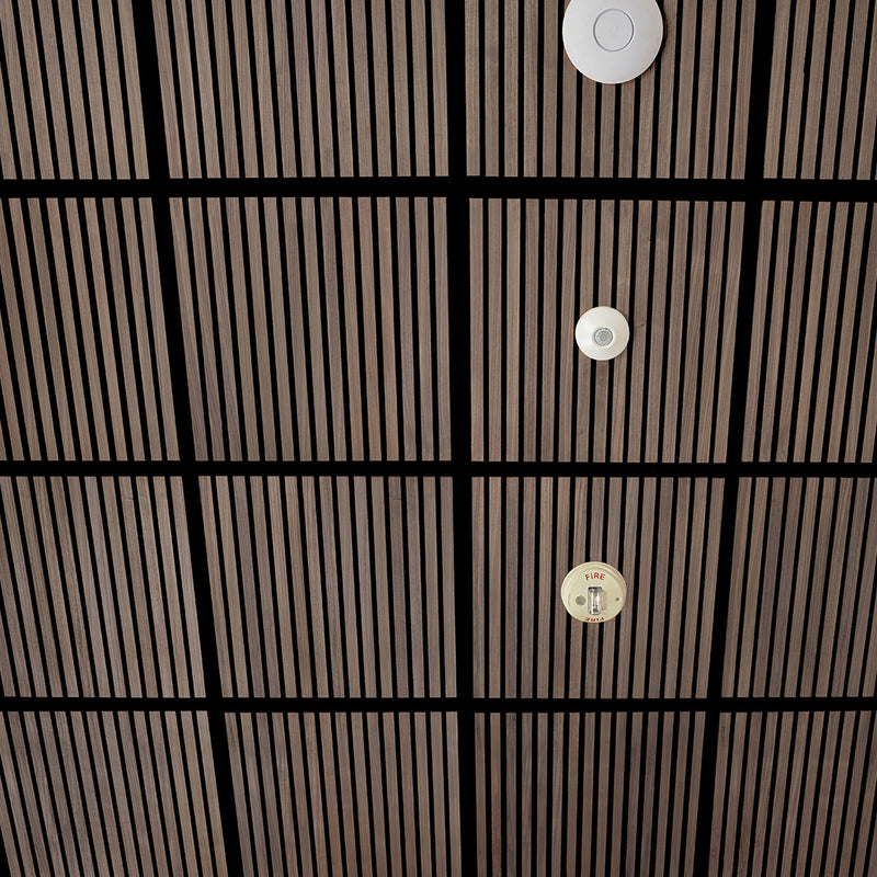 A close-up view of a modern ceiling with a grid of dark wood slats and black beams, featuring three circular white and beige ceiling-mounted fixtures.