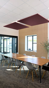 Two burgundy square ceiling-mounted acoustic baffles suspended above a conference table in an office space.
