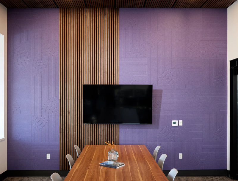 A modern conference room featuring a purple textured wall with a vertical wood slat accent panel and a mounted flat-screen TV above a wooden table with chairs.