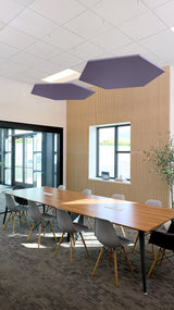 Two dark blue hexagonal ceiling baffles suspended above a conference table in an office space with wood paneling.