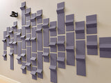Three-dimensional purple and gray tiles arranged in an ascending pattern on a beige wall with a clock visible on the left.
