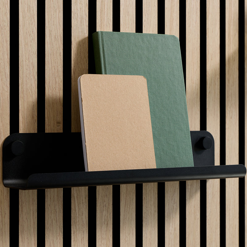 Black shelf with rounded ends mounted on vertical wood slats, holding two fabric-covered books in tan and sage green.