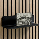 Black metal shelf with curved edges mounted on vertical wood slat wall, holding a black and white photograph.