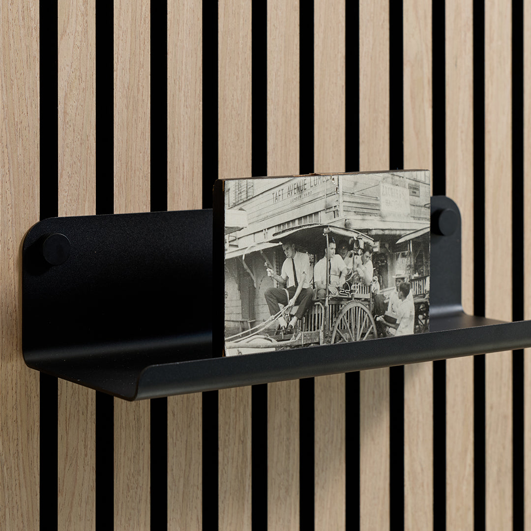Black metal shelf with curved edges mounted on vertical wood slat wall, holding a black and white photograph.