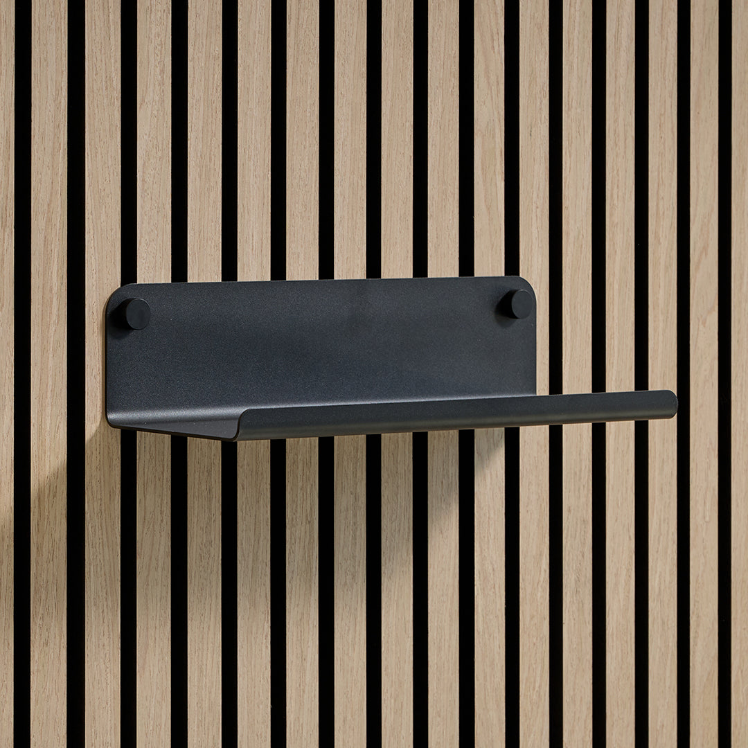 A matte black metal wall-mounted shelf with a rectangular backplate and a single horizontal shelf, shown against a light wood slat wall.