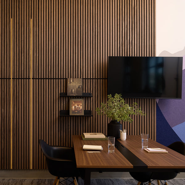 A modern interior scene with a dark wood slatted accent wall, a mounted black TV, small floating shelves, books, and a potted plant above a wooden table with chairs.