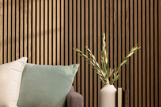 Felt Right Walnut Wood Slat Wall Panel in a living room behind a couch with leaves in a vase in the foreground.
