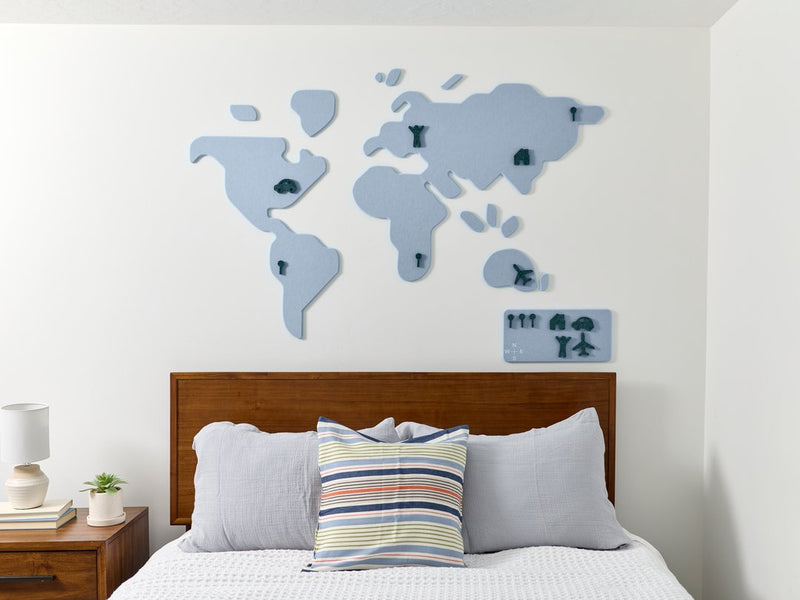 World map wall decoration on a white wall above a bed with pillows.