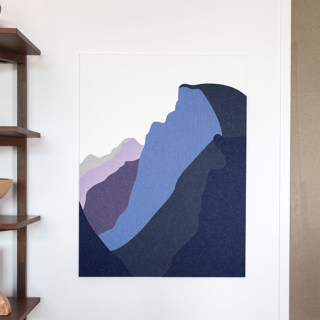 Abstract mountain art print on a white wall next to a wooden shelf.