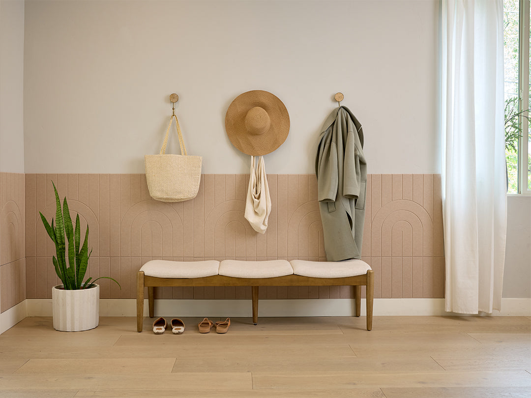 Entryway with a wooden bench, coat, bag, and hat against a wall with Felt Right wall design in a shade of beige.