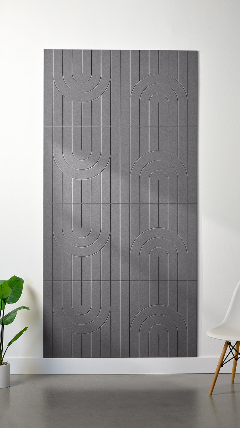 Grey Felt Right 4’ x 8’ PET felt panel with a linear and curvy pattern engraved into the material against a white wall. A plant and chair are in the foreground.