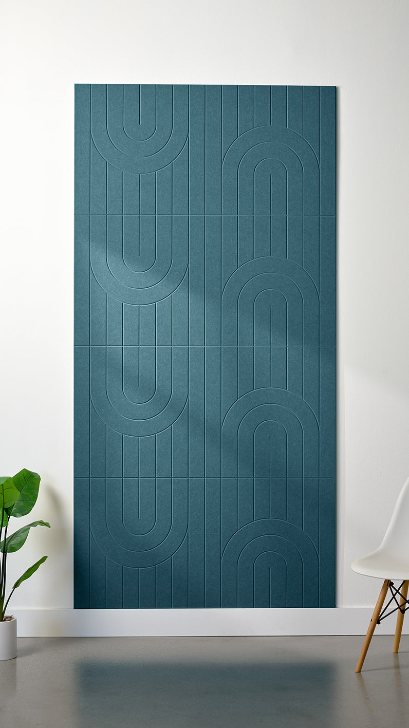 Blue Felt Right 4’ x 8’ PET felt panel with a linear and curvy pattern engraved into the material against a white wall. A plant and chair are in the foreground.