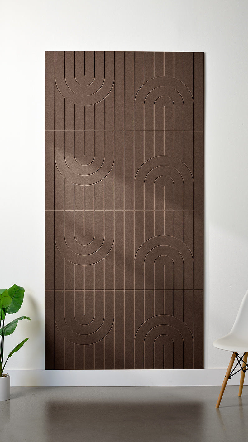 Brown Felt Right 4’ x 8’ PET felt panel with a linear and curvy pattern engraved into the material against a white wall. A plant and chair are in the foreground.