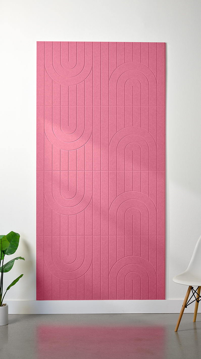 Hot pink Felt Right 4’ x 8’ PET felt panel with a linear and curvy pattern engraved into the material against a white wall. A plant and chair are in the foreground.