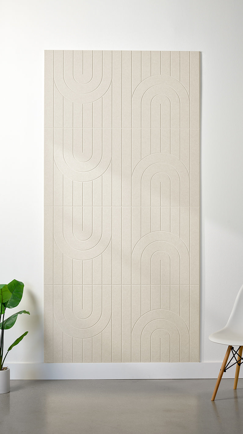Ivory Felt Right 4’ x 8’ PET felt panel with a linear and curvy pattern engraved into the material against a white wall. A plant and chair are in the foreground.