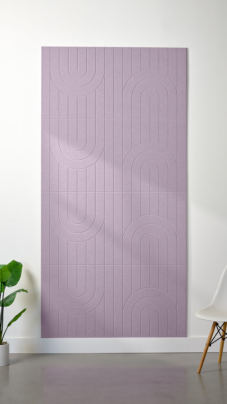Pale purple Felt Right 4’ x 8’ PET felt panel with a linear and curvy pattern engraved into the material against a white wall. A plant and chair are in the foreground.