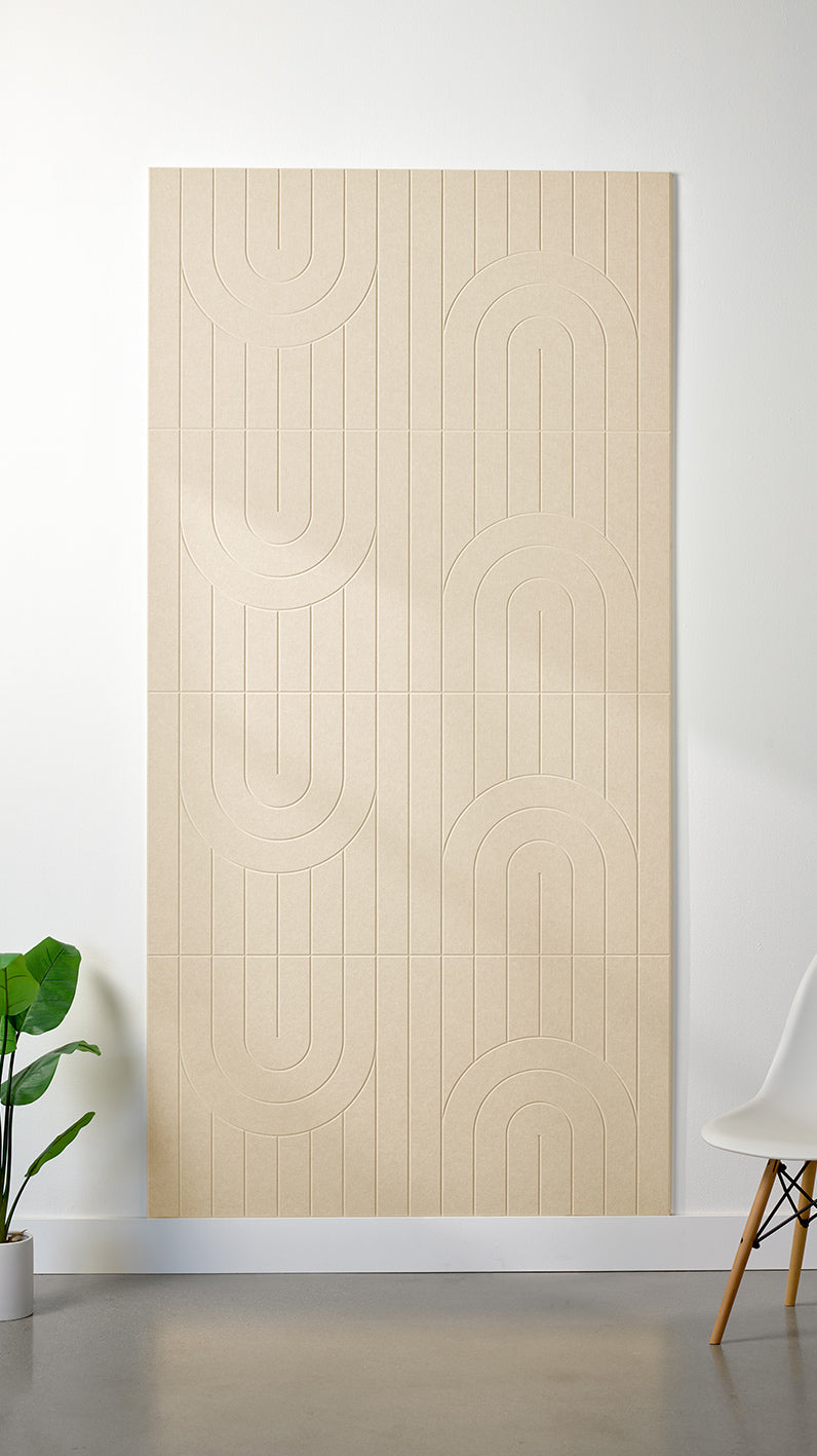Light beige Felt Right 4’ x 8’ PET felt panel with a linear and curvy pattern engraved into the material against a white wall. A plant and chair are in the foreground.