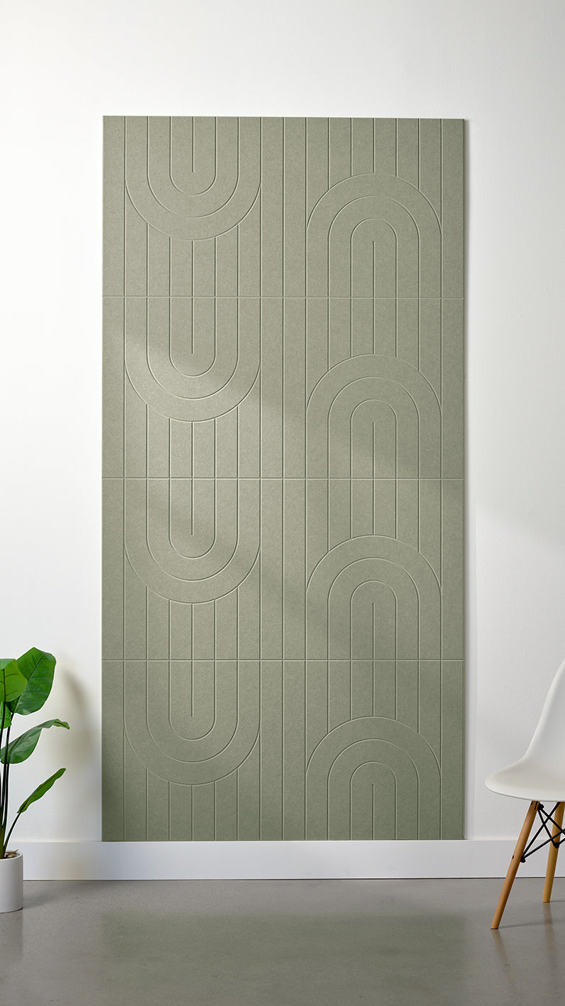 Sage green Felt Right 4’ x 8’ PET felt panel with a linear and curvy pattern engraved into the material against a white wall. A plant and chair are in the foreground.