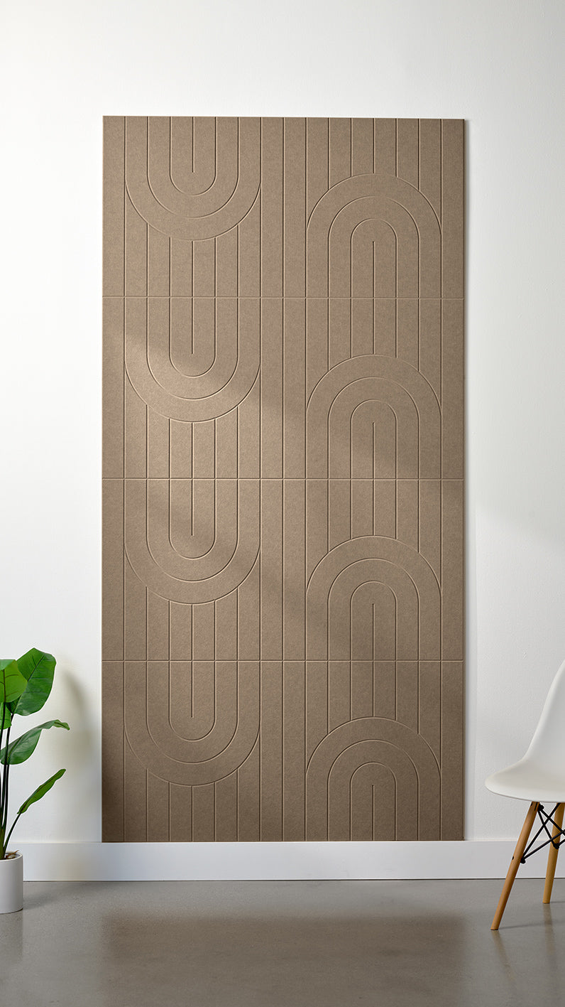Brown Felt Right 4’ x 8’ PET felt panel with a linear and curvy pattern engraved into the material against a white wall. A plant and chair are in the foreground.